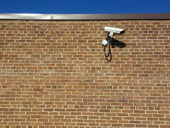 Low angle view of security camera on brick wall