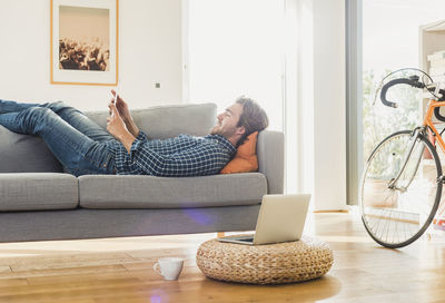 Young man lying on the couch at home looking at digital tablet
