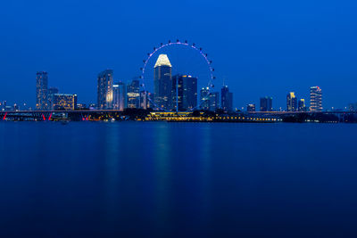 Singapore flyer by bay of water against clear blue sky in city