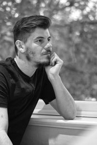 Young man looking away while sitting by window