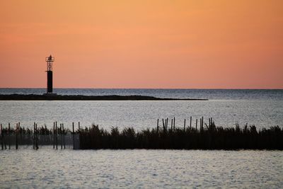 Lighthouse by sea against sky during sunset
