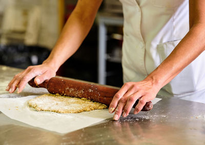 Crop unrecognizable pastry chef rolling shortcrust dough on baking paper while preparing cookies in kitchen