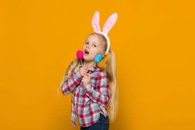 Portrait of young woman holding toy against yellow background