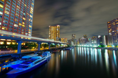 Illuminated bridge over river by buildings against sky at night