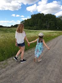 Rear view of mother and daughter walking on road amidst grassy field