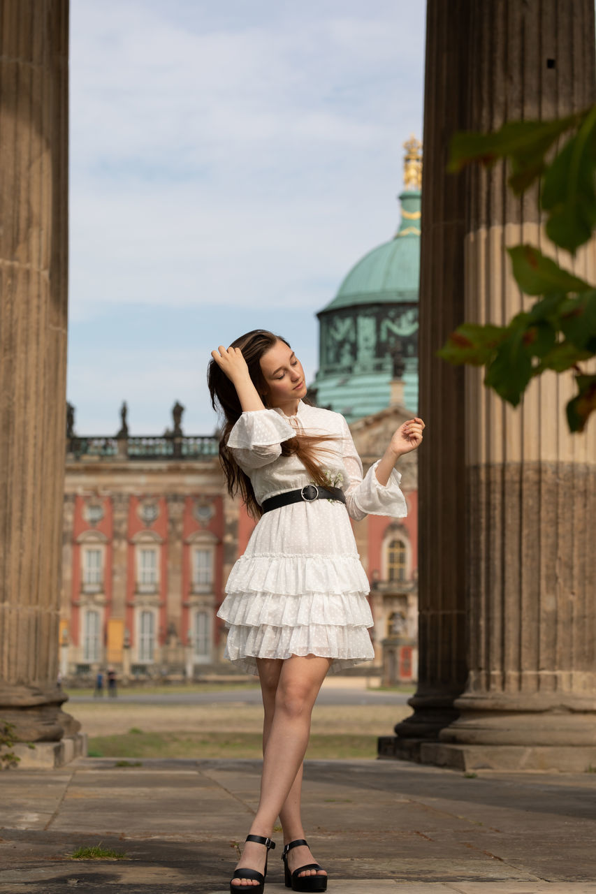 FULL LENGTH OF WOMAN STANDING AGAINST BUILDING
