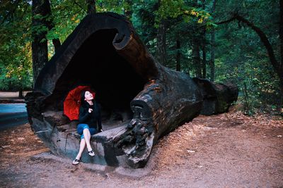 Woman sitting on fallen tree with red umbrella