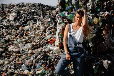 Portrait of young woman standing against garbage heap