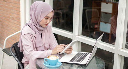 Woman wearing hijab using digital tablet at sidewalk cafe