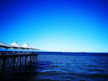 Pier over sea against clear blue sky