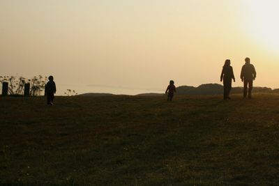 People walking on field against sky during sunset