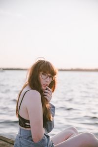 Young woman sitting in sea against sky