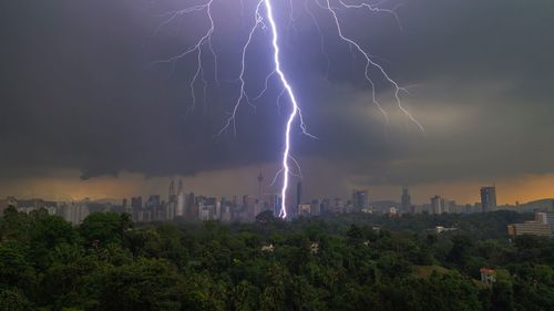 Low angle view of lightning over cityscape against dramatic sky