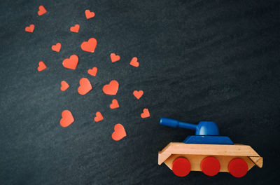 Directly above shot of toy tank firing red heart shapes on black table