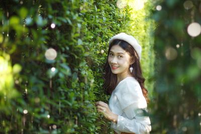 Portrait of smiling young woman standing against trees