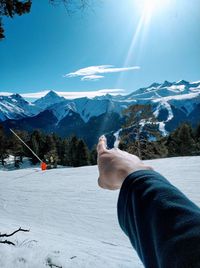 Cropped hand of person pointing towards snowcapped mountain against sky