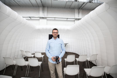 Portrait of mature man with camera standing in room