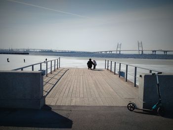 Rear view of parent crouching by baby on pier against sky during winter