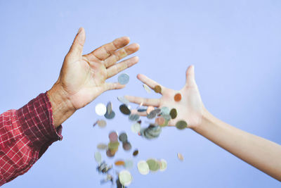 Cropped image of father and son dropping coins against purple background