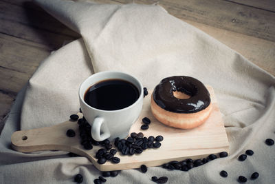 High angle view of roasted coffee beans with chocolate donut and black coffee cup on wooden table