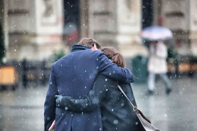 Rear view of couple embracing in city during snowfall