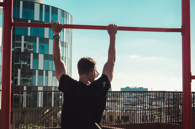 Man hanging on pole while standing by railing in city