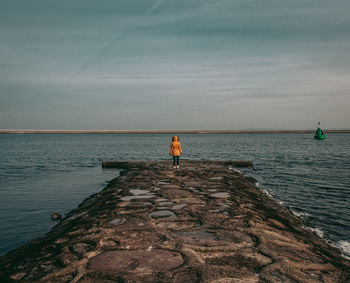 Rear view of woman standing by sea on groyne