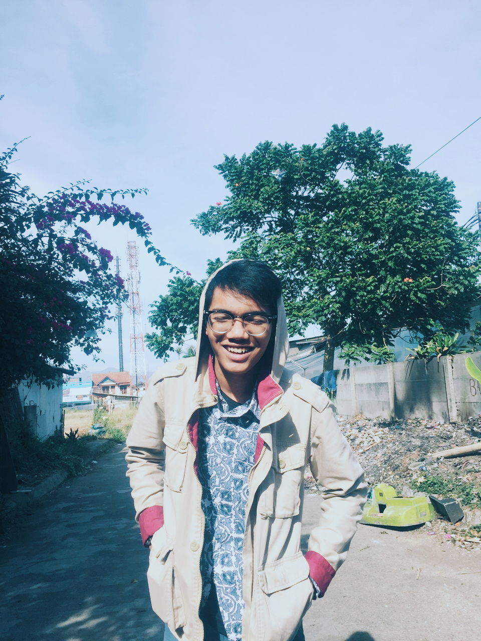 one person, smiling, happiness, young adult, front view, spring, portrait, blue, tree, adult, nature, looking at camera, emotion, plant, lifestyles, glasses, standing, leisure activity, teeth, smile, cheerful, day, sky, casual clothing, clothing, outdoors, city, fashion, women, eyeglasses, architecture, enjoyment, three quarter length, sunlight, fun, waist up, cool attitude, laughing, carefree