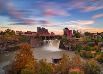 Scenic view of river by city against sky during sunset