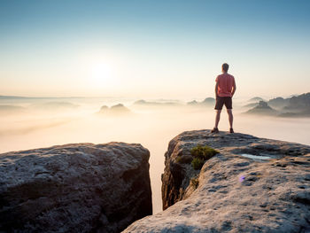 Tourist or hiker on the peak of high rocks watching morning mist in landscape. sport and active life