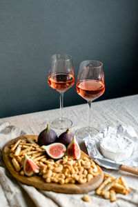 Rose wine with ripe figs, camembert cheese, and cashews on a table indoors.