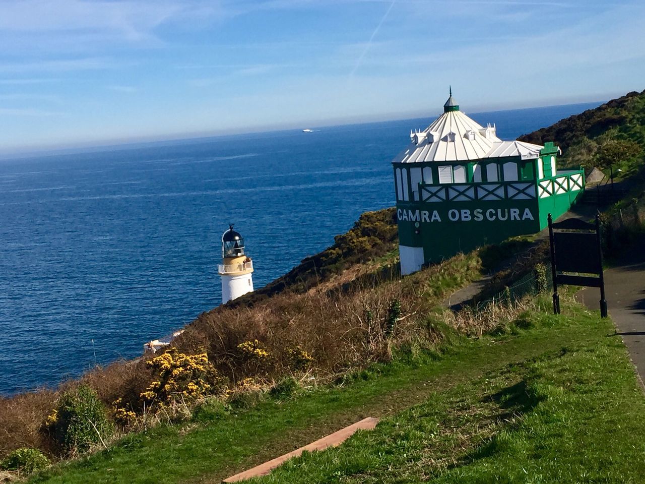 sea, lighthouse, text, sky, cloud - sky, water, horizon over water, tranquility, protection, building exterior, grass, outdoors, scenics, architecture, no people, nature, day