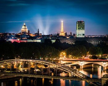 Illuminated bridge over river by buildings against sky at night