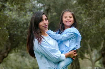Portrait of mother carrying daughter against tree at park
