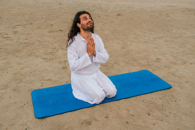 Young man looking away while sitting on sand