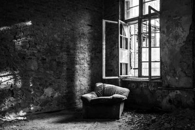 Old sofa against open window in abandoned room