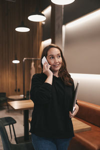 Adult business woman freelancer works using wireless technology talking on the phone sitting in cafe