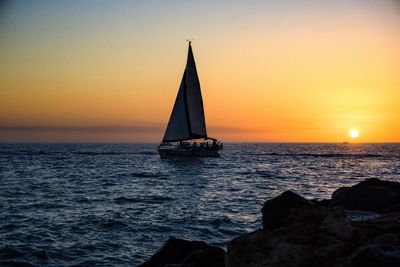 Silhouette of sailboat in sea during sunset