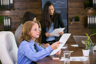 Businesswoman analyzing document at desk colleague in background