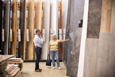 Woman talking to senior man while shopping laminated boards at hardware store