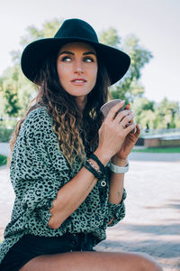 Portrait of beautiful stylish young woman wearing black felt hat drinking coffee. 