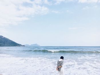 Rear view of man walking at beach against sky