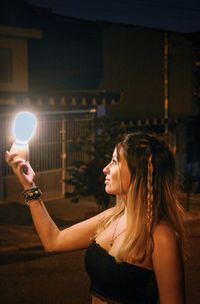 Side view of young woman holding illuminated lighting equipment at night