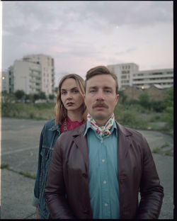 Portrait of young couple standing against buildings in city