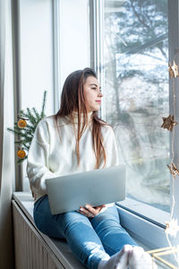 Young woman using mobile phone while sitting on bed at home