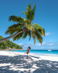 Rear view of woman walking on beach against clear blue sky