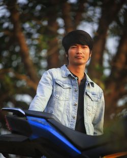 Portrait of young man standing by motorcycle outdoors