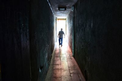 Rear view of man walking in alley amidst buildings