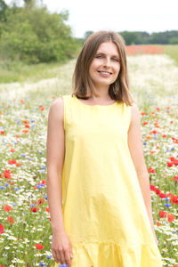 A beautiful young blonde woman in a yellow dress stands among a flowering field