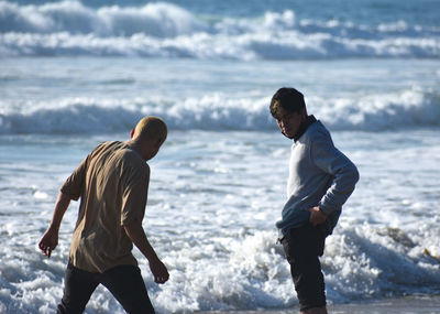Rear view of men standing at beach